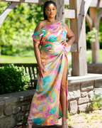Woman wearing a colorful one-shoulder dress standing outdoors with greenery in the background