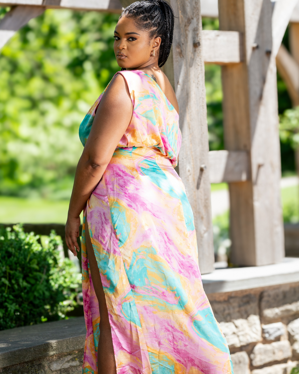 Woman wearing a colorful tie-dye dress standing outdoors with greenery in the background