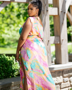 Woman wearing a colorful tie-dye dress standing outdoors with greenery in the background