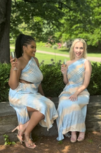 Two women in matching light blue and white dresses sitting outdoors.