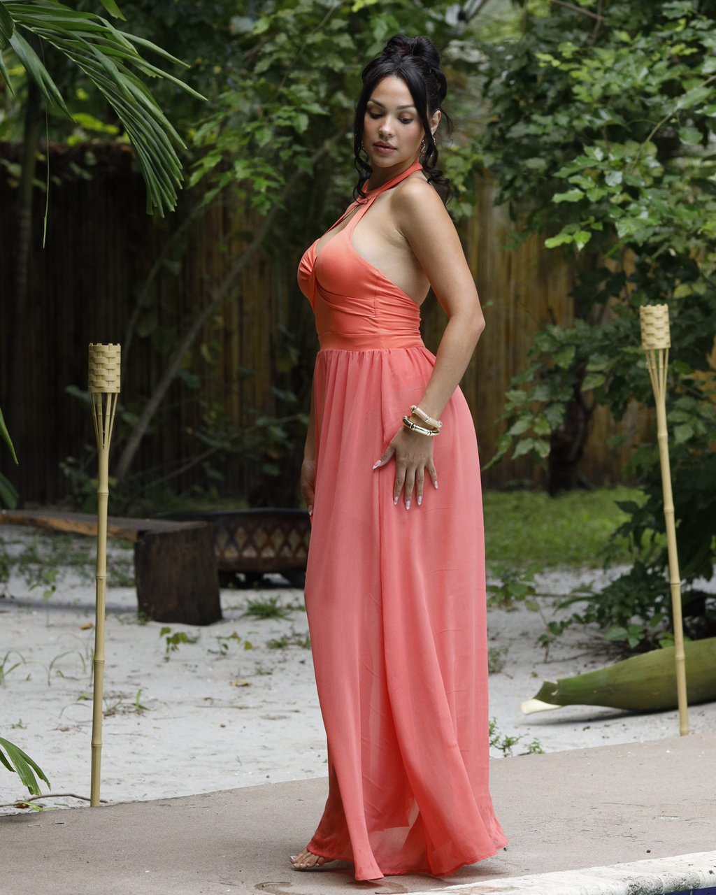 Woman in a coral dress standing outdoors with greenery in the background