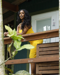 Woman in a yellow dress standing on a wooden deck with plants around.
